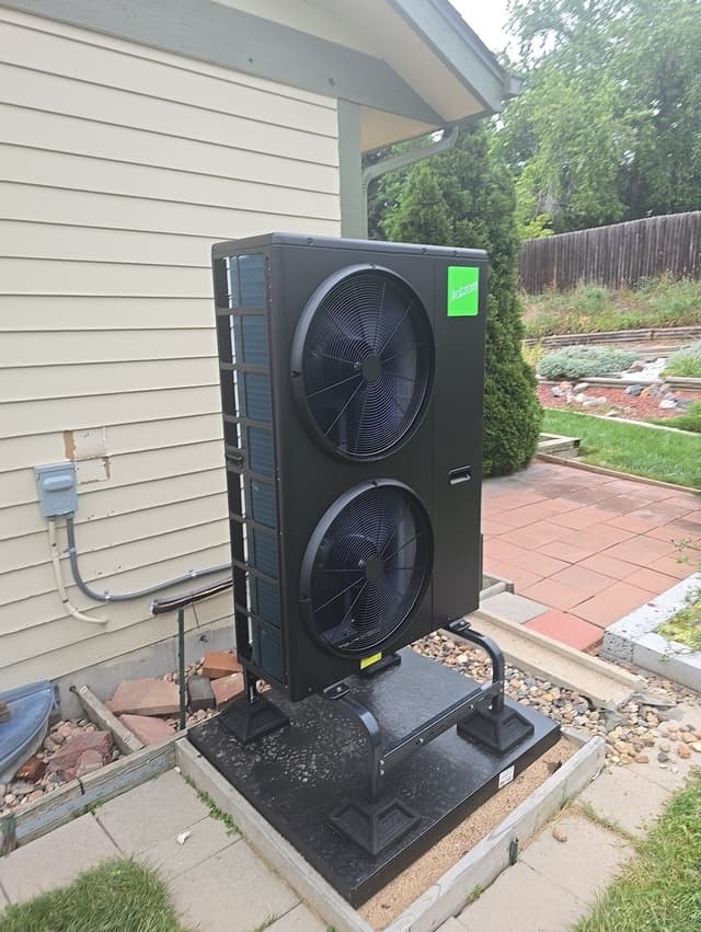 4-ton Jetson Air central ducted heat pump mounted on a pad beside a house in Aurora, CO, with electrical conduit, disconnect box, gravel, pavers, and landscaped garden beds visible.