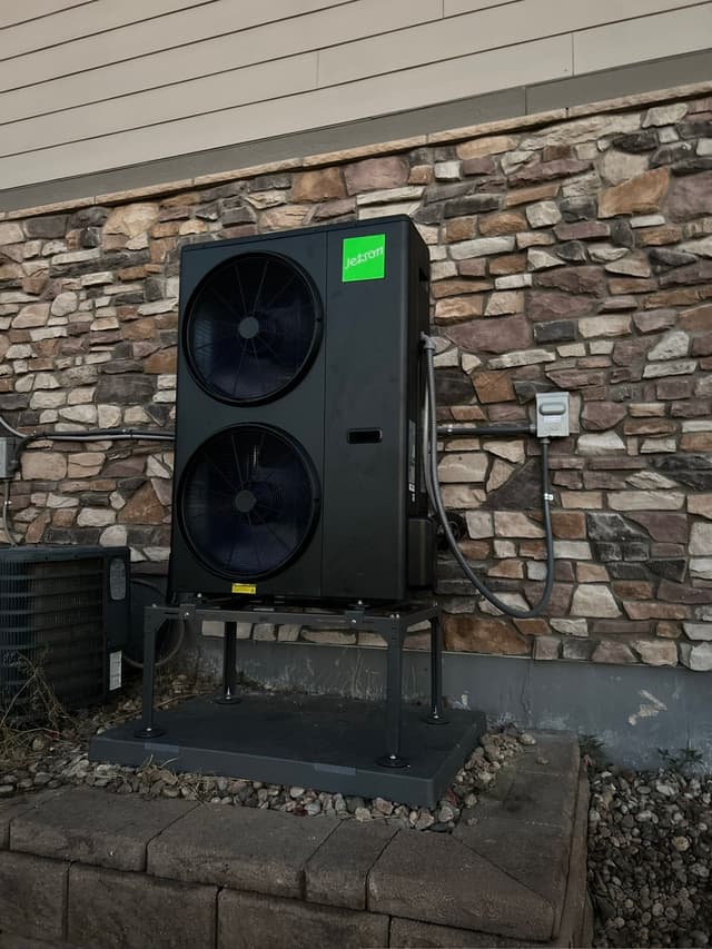 4-ton Jetson Air dual-fan outdoor heat pump unit mounted against a decorative stacked-stone exterior wall in Aurora, with electrical conduit and refrigerant lines running neatly to a wall-mounted disconnect box.