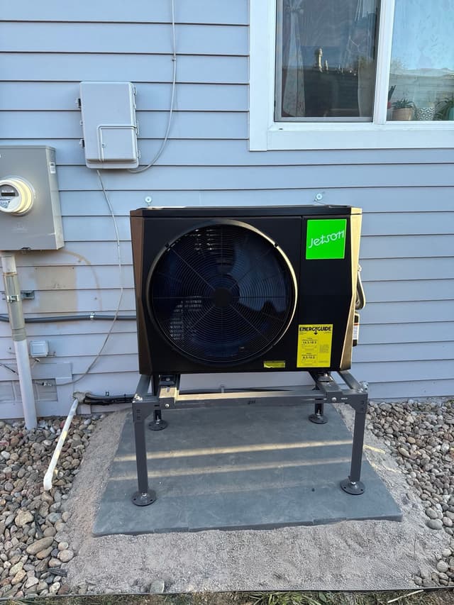 Jetson Air 2-ton central ducted heat pump installed against light-blue vinyl siding of a home in Aurora, with utility meter and electrical disconnect visible to the left.