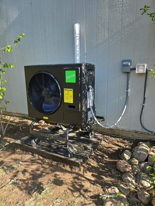 Jetson Air 3-ton heat pump on an elevated metal stand against a grey-sided house in Boulder, Colorado, with line set and disconnect box visible on the wall.