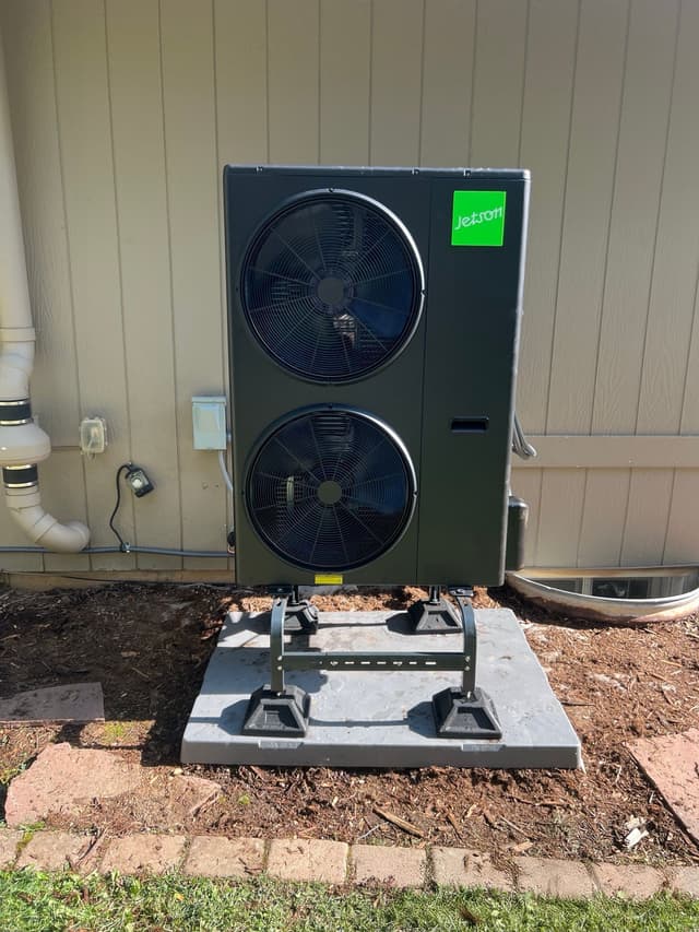 Black Jetson Air 4-ton heat pump outdoor unit installed in a mulched side yard against cream vertical-board siding in Boulder, Colorado.