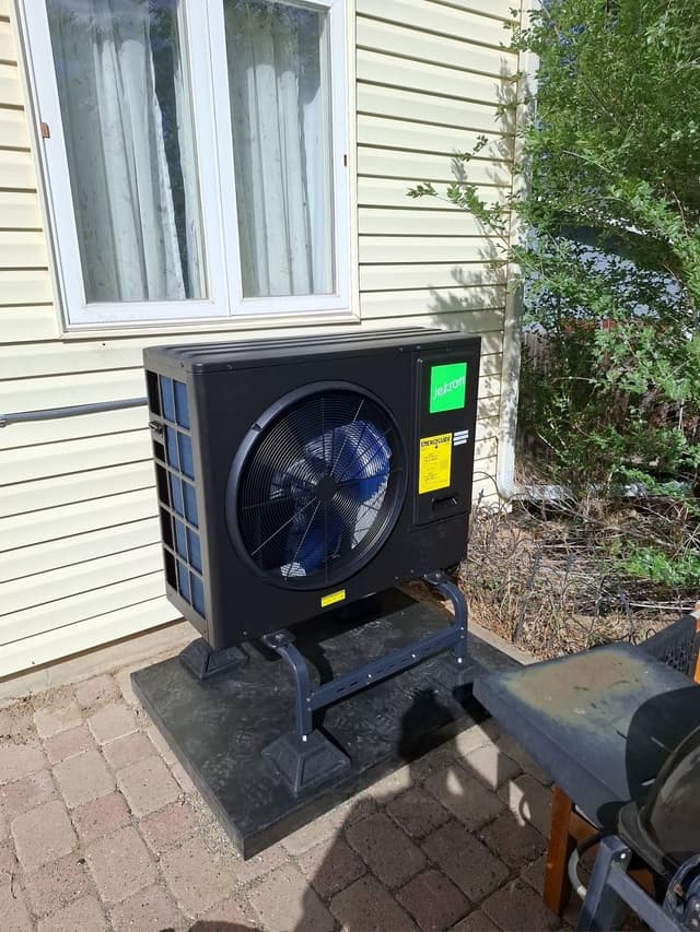 Jetson Air 3-ton heat pump mounted on a metal stand over a rubber pad on a brick paver patio beside a vinyl-sided house in Broomfield, CO.