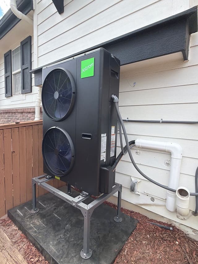 A black Jetson Air 4-ton heat pump installed along the side of a house in Commerce City, with refrigerant lines and conduit running neatly into the wall.