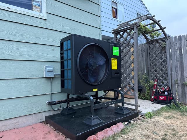 Jetson Air 3-ton heat pump mounted on a raised black equipment stand against light-green siding of a Denver home, with line sets running neatly to a wall disconnect box.