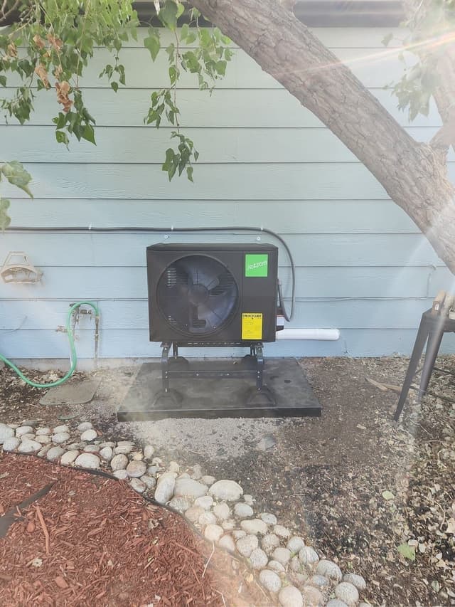 Black Jetson Air 2-ton central ducted heat pump installed along the side of a light-blue-sided Denver home, with electrical conduit running along the wall above the unit.