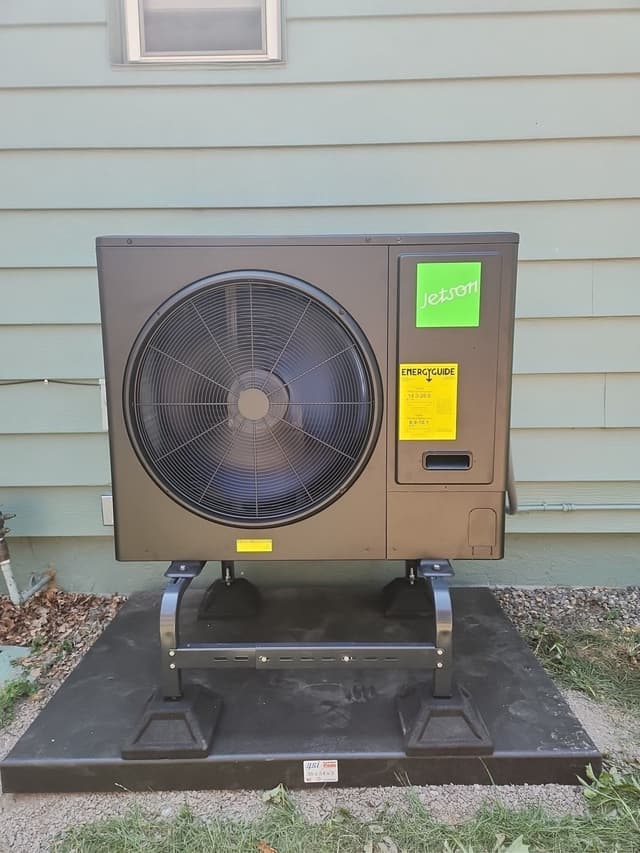 Jetson Air 3-ton central ducted heat pump outdoor unit mounted against light teal vinyl siding of a Denver home, with EnergyGuide sticker visible.