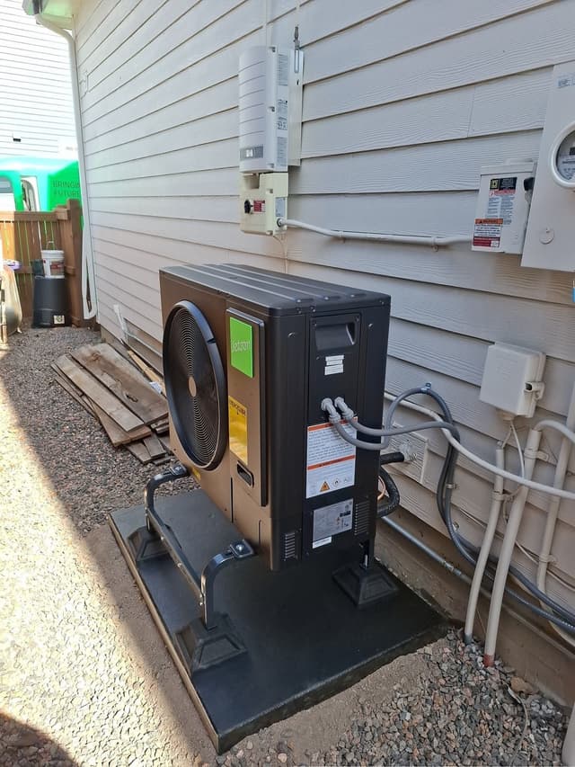Jetson Air 3-ton central ducted heat pump mounted along the side of a Denver home with light gray lap siding, refrigerant lines and conduit running up the wall to the disconnect box and electrical panel.