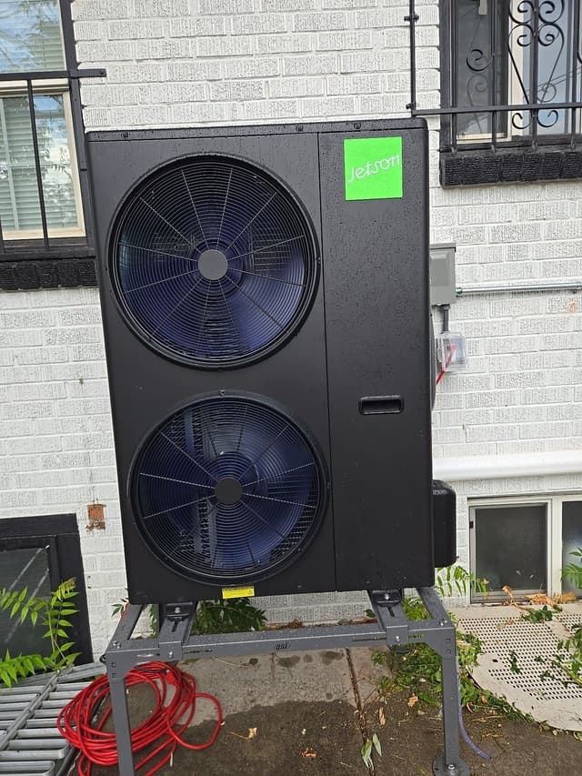 A large black Jetson Air 4-ton heat pump outdoor unit mounted against a white brick wall at a Denver home.