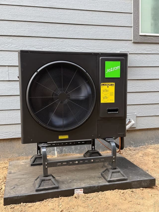 Jetson Air 3-ton outdoor heat pump unit on an elevated stand over a rubber pad, mounted against gray lap siding of a Denver home.