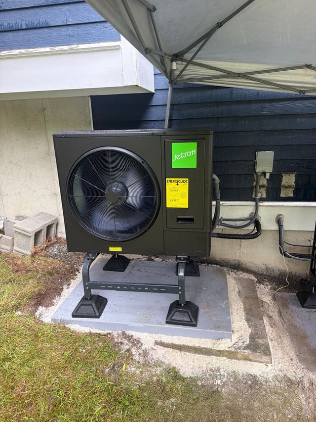 Jetson Air 3-ton central ducted heat pump condenser installed alongside a house with dark blue siding in Dunstable, MA, with refrigerant lines running neatly along the wall.