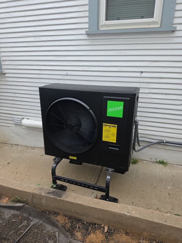 Jetson Air 3-ton heat pump mounted on a ground stand beside a house with white lap siding in Englewood, Colorado, with refrigerant lines running along the foundation.