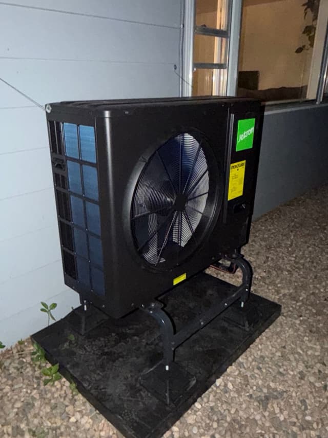 Jetson Air 4-ton heat pump condenser unit on a raised equipment pad against the grey siding of a Fort Collins home, photographed at night.