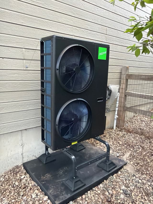 A black Jetson Air 4-ton heat pump mounted on a pad stand over gravel against light gray lap siding on a Fort Collins, CO home.