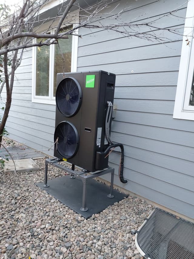 A black Jetson Air 4-ton heat pump mounted against gray lap siding at a Fort Collins home, with refrigerant lines and conduit running neatly to a disconnect box.
