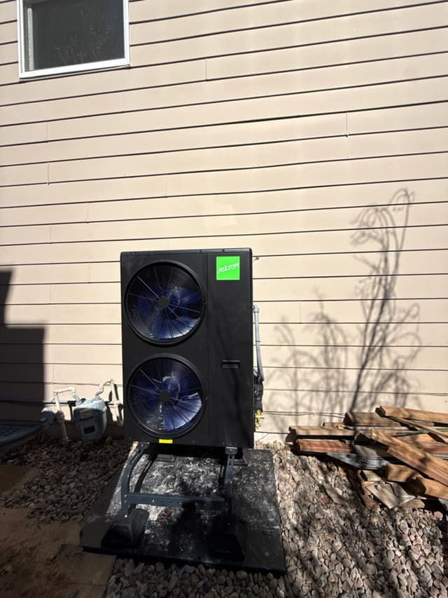 4-ton dual-fan outdoor heat pump unit mounted on a metal stand over a concrete pad against tan house siding in Fort Collins, CO.