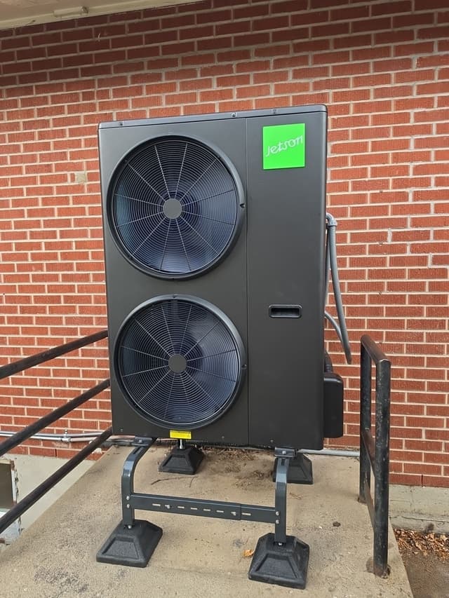 4-ton Jetson Air dual-fan heat pump condenser installed beside a brick building in Golden, with conduit running along the side and metal stair railings visible on either side.