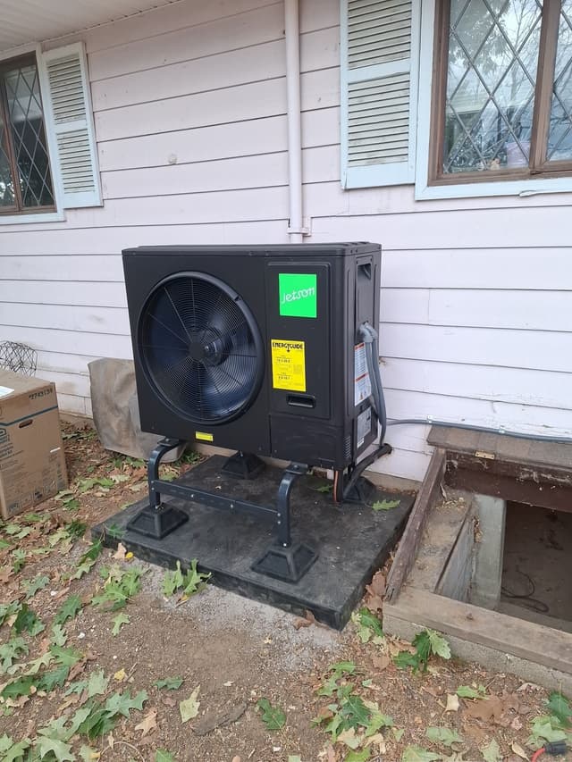 Jetson Air 3-ton central ducted heat pump installed on a metal stand beside a white-sided house in Lafayette, Colorado, with conduit running up the wall and fallen leaves on the ground.