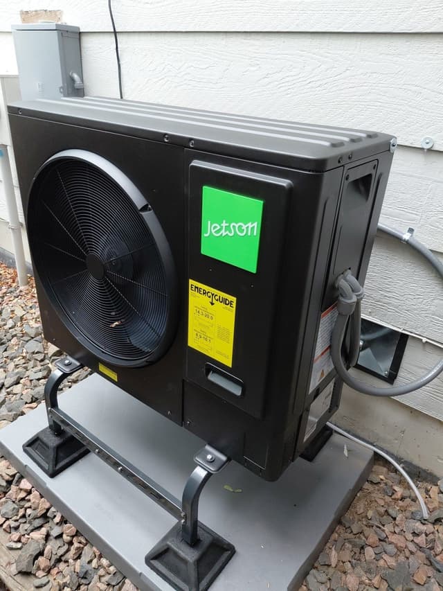 Black Jetson Air 3-ton central ducted heat pump installed on the side of a white-sided house in Lafayette, CO, with conduit and line set running neatly into the home.