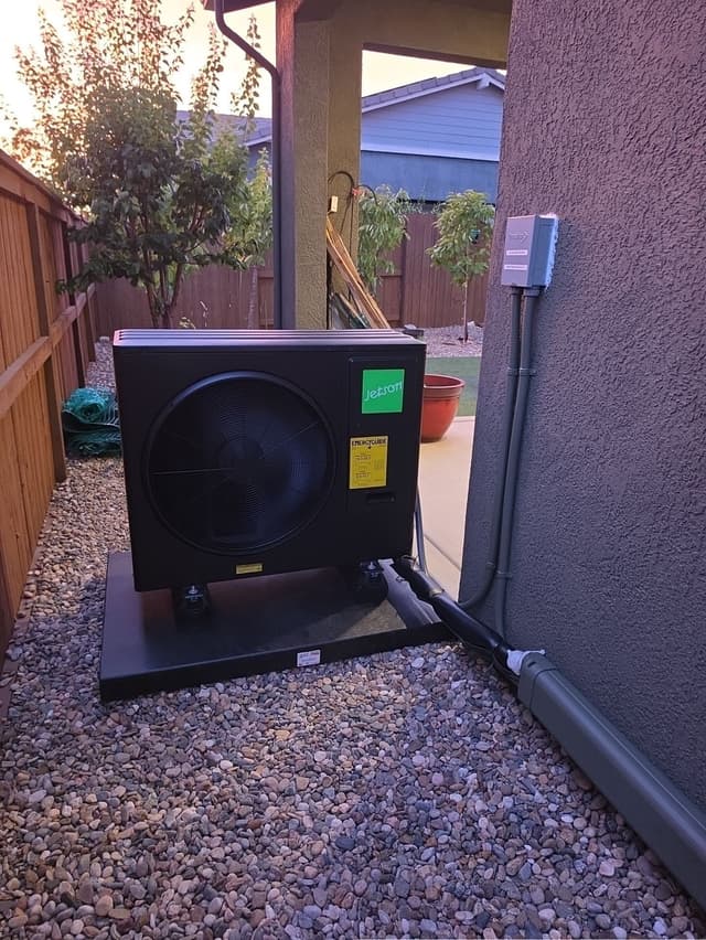 Black Jetson Air 3-ton heat pump installed in a narrow gravel side yard against a stucco wall in Lincoln, California, with conduit runs and disconnect box visible, install complete.