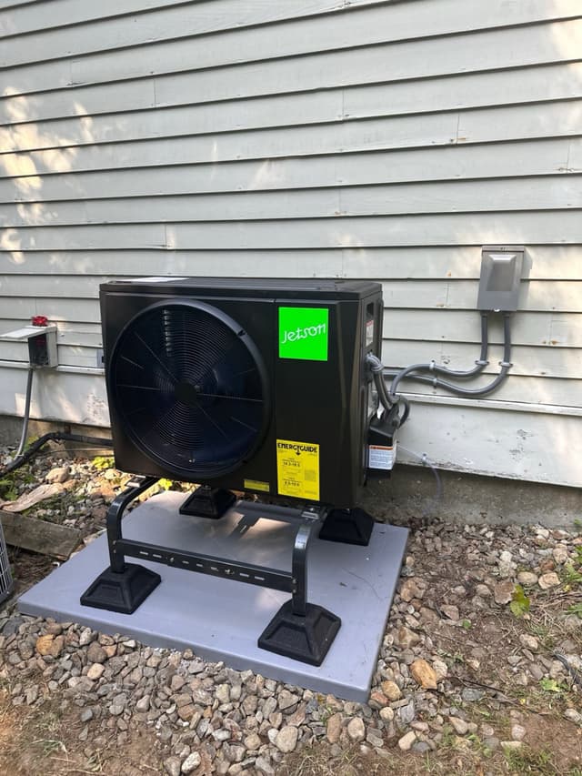 Jetson Air 2-ton outdoor heat pump unit installed alongside a house in Lincoln, MA, with gray conduit running to a disconnect box on white vinyl siding.