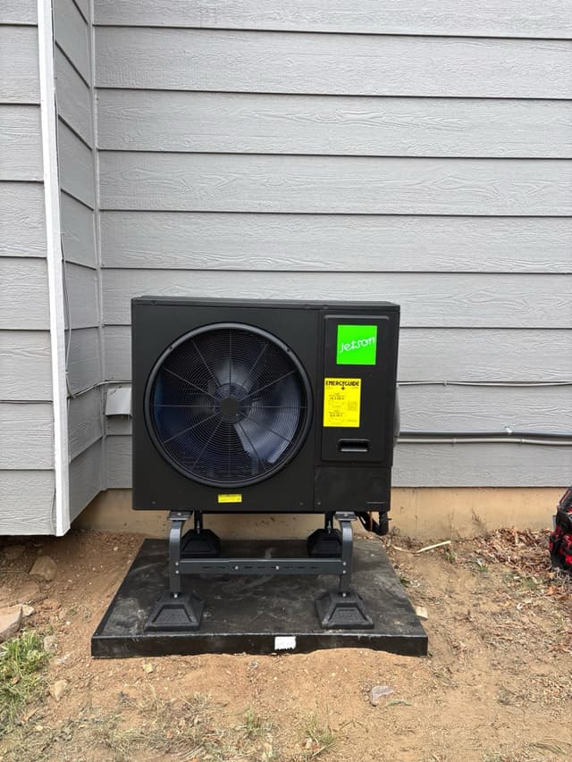 Jetson Air 3-ton heat pump mounted on an anti-vibration pad against gray lap siding of a home in Littleton, CO, with refrigerant lines running along the exterior wall.