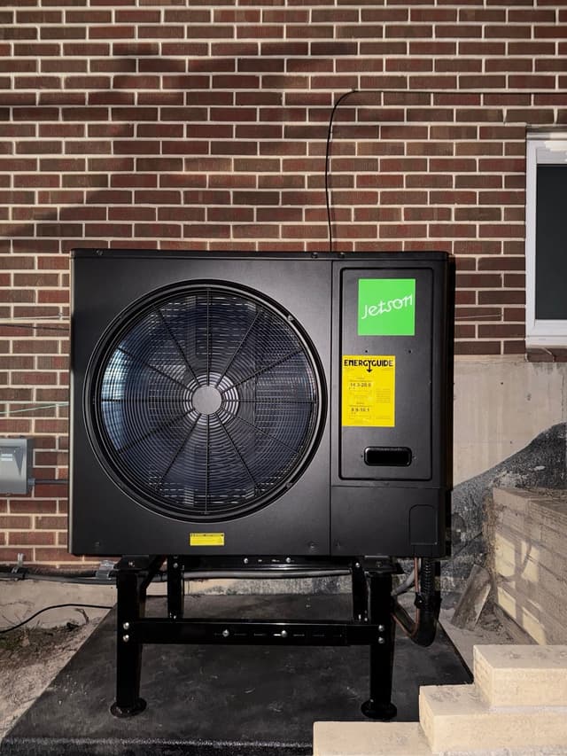 Jetson Air 3-ton central ducted heat pump mounted against a red brick exterior wall at a home in Littleton, MA.