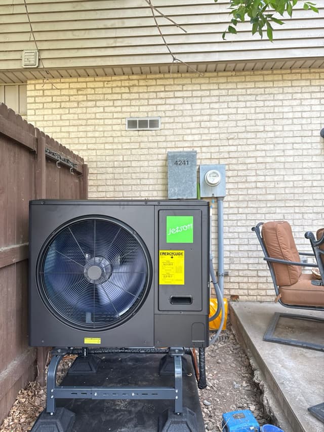 Jetson Air 3-ton heat pump mounted on a metal stand in a narrow side yard between a wood fence and brick house exterior in Littleton, CO.