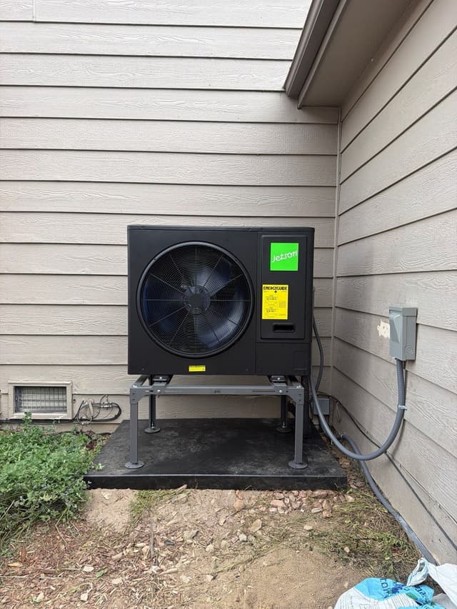 Jetson Air 3-ton central ducted heat pump installed on the side of a light-gray vinyl-sided house in Littleton, with electrical conduit running to a disconnect box on the wall.