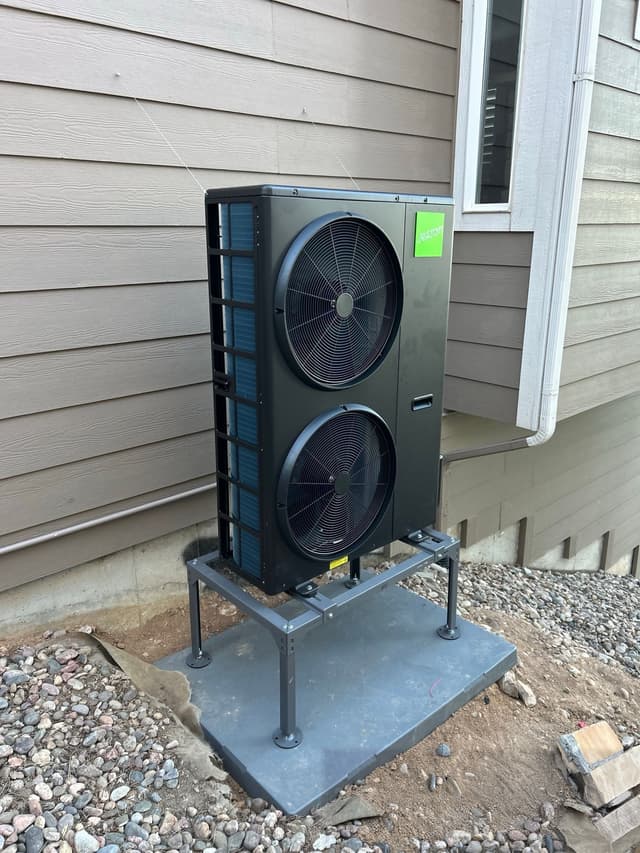 Black Jetson Air 4-ton heat pump installed along the side of a gray lap siding home in Littleton, MA.