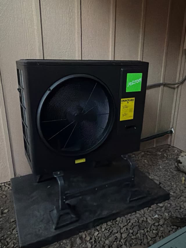 Jetson Air 3-ton heat pump outdoor unit on a gravel pad against tan vertical siding at a home in Littleton, CO.