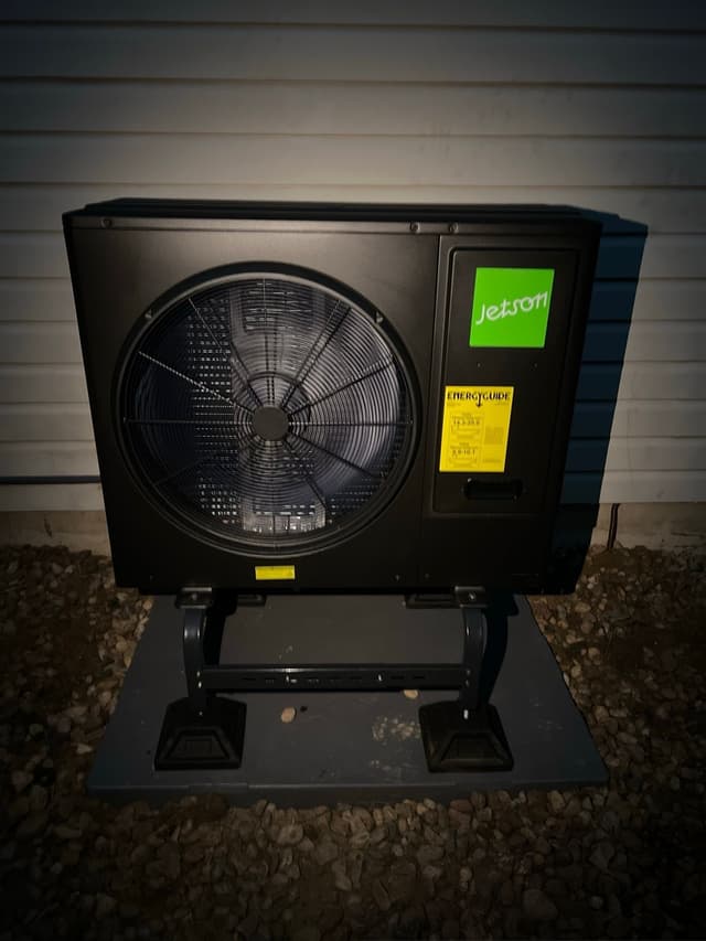 Jetson Air 3-ton heat pump condenser installed against white vinyl siding on a Longmont home, photographed at night.