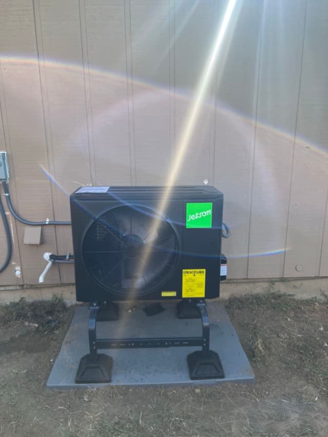 Jetson Air 2-ton central ducted heat pump unit installed against tan vertical-board siding at a Longmont home, with refrigerant lines and conduit running to a disconnect box.