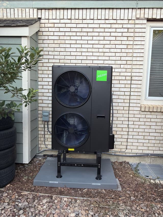 4-ton Jetson Air dual-fan outdoor heat pump condenser mounted on a metal riser stand against a light brick exterior wall at a home in Longmont, CO.