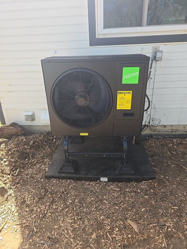 Jetson Air 3-ton heat pump condenser mounted on a black equipment pad alongside a white-sided house in Louisville, Colorado, with refrigerant lines and electrical conduit running to a disconnect box on the wall.