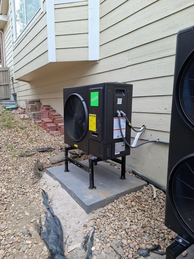 Two black Jetson Air heat pump outdoor units installed along the side of a tan-sided house in Louisville, CO, with gravel landscaping and stacked brick pavers in the background.