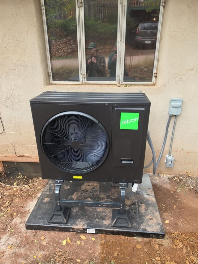 Jetson Air 3-ton central ducted heat pump installed against a tan stucco exterior wall in Manitou Springs, Colorado, with electrical disconnect box and conduit visible.