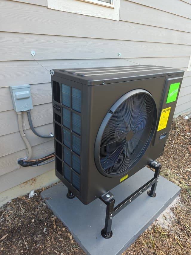 Jetson Air 3-ton outdoor heat pump unit mounted on a metal stand on a concrete pad against tan lap siding, with refrigerant lines and a disconnect box visible, in Monument, CO.