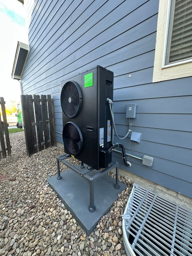 5-ton Jetson Air central ducted heat pump mounted on an elevated stand against gray lap siding at a home in Parker, CO, with line set and conduit running neatly to a disconnect box.