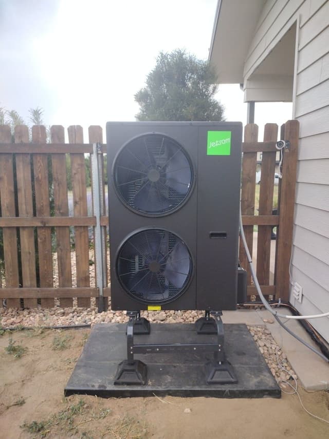 Black Jetson Air 4-ton heat pump installed in a gravel side yard next to a light-gray-sided home in Parker, CO, with refrigerant lines running neatly along the wall and a wooden privacy fence behind it.