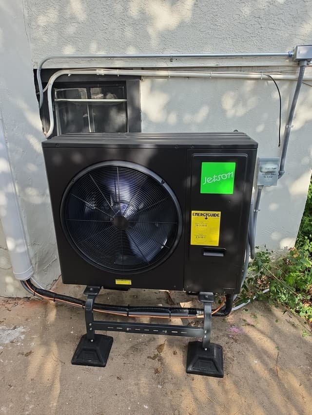 Jetson Air 3-ton central ducted heat pump mounted on a metal stand against a stucco exterior wall in Pueblo, Colorado, with refrigerant lines and conduit running neatly along the wall and a disconnect box visible to the right.