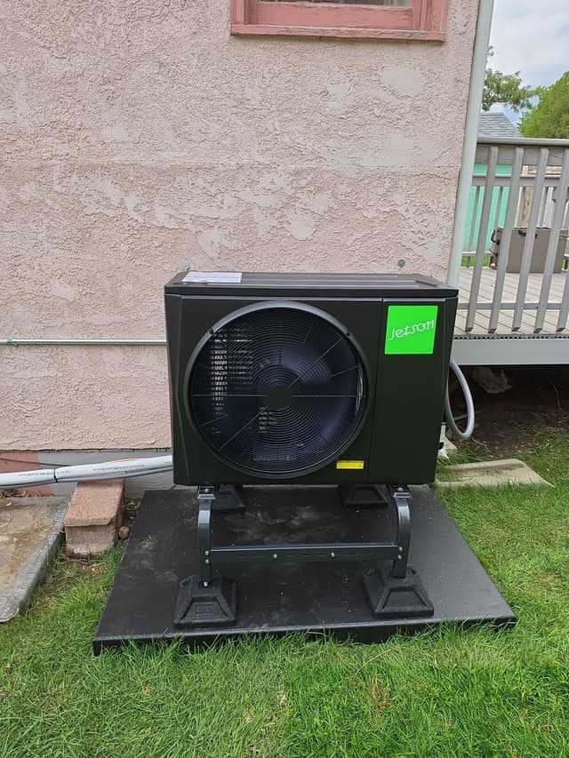 Black Jetson Air 2-ton heat pump condenser installed on a grassy lawn beside a stucco house wall in Pueblo, Colorado.