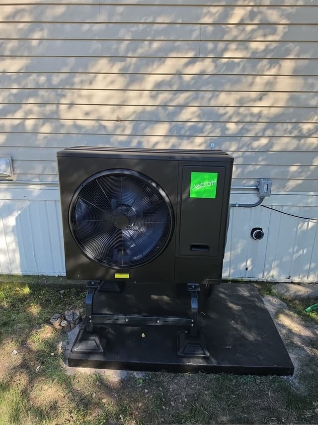 Jetson Air 3-ton heat pump installed in the side yard of a home with beige horizontal siding in Pueblo West, CO, with electrical conduit and disconnect box visible on the wall.