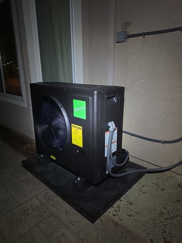 Black Jetson Air 3-ton heat pump condenser installed on a patio against a stucco exterior wall in Rocklin, CA, photographed at night with refrigerant lines running to the electrical disconnect.