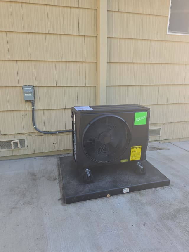 2-ton Jetson Air central ducted heat pump installed on a concrete surface beside a tan wood-sided building in College/Glen, Sacramento, with electrical disconnect and conduit visible on the wall.