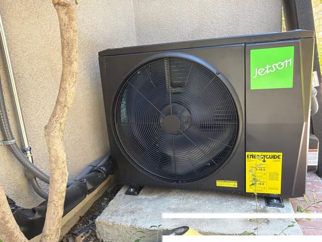 Black Jetson Air 2-ton central ducted heat pump condenser installed against a light stucco exterior wall in Valencia, Santa Clarita, CA.