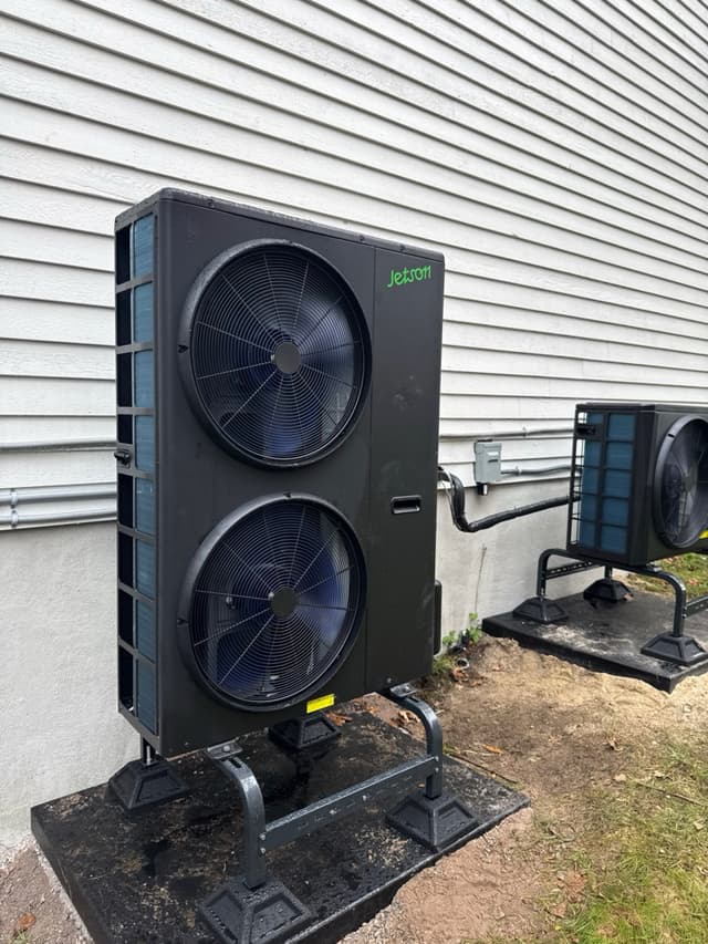 Two black Jetson Air heat pump outdoor units installed side by side on riser stands against white vinyl siding of a home in Stoneham, MA.
