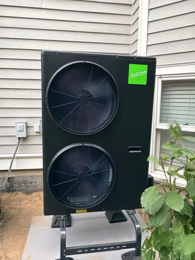 Black Jetson Air dual-fan 4-ton heat pump mounted against gray vinyl siding at a Sudbury, MA home.