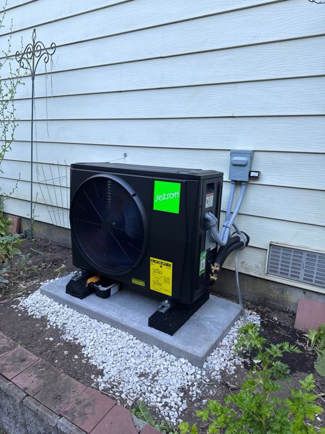 Jetson Air 2-ton heat pump condenser mounted on a concrete pad with white decorative gravel against light grey vinyl siding of a home in Semiahmoo Town Centre, Surrey BC.