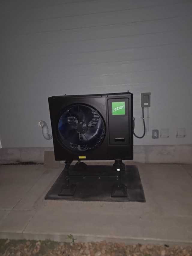 Jetson Air 3-ton central ducted heat pump unit mounted on a stand against the side of a house in Thornton, photographed at night.