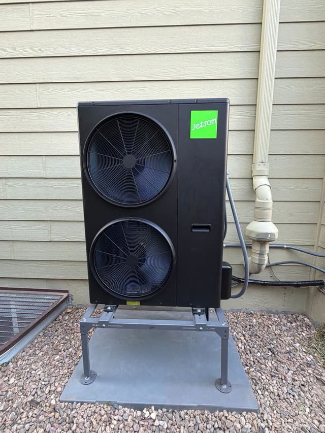 5-ton Jetson Air central ducted heat pump installed on the side of a tan lap-siding house in Timnath, Colorado, with conduit and refrigerant lines running neatly along the wall.
